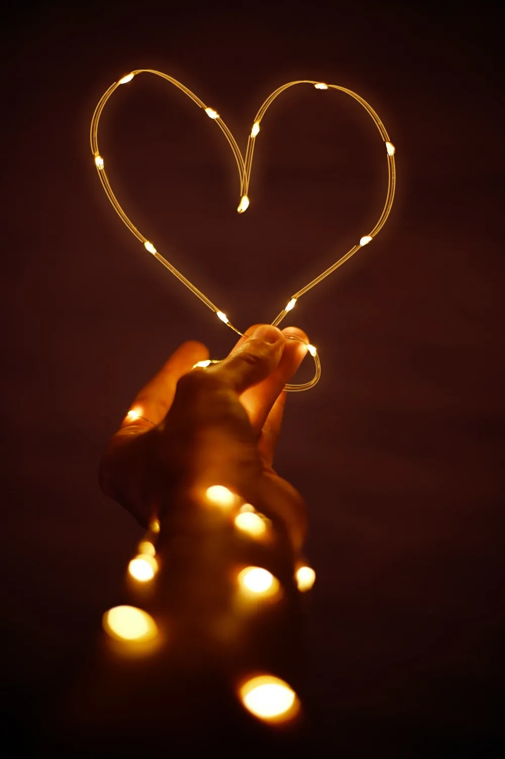 A hand holding fairy lights in a shape of a heart